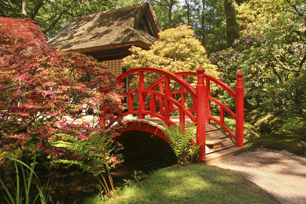 Japanese garden with bright red bridge over a small stream.